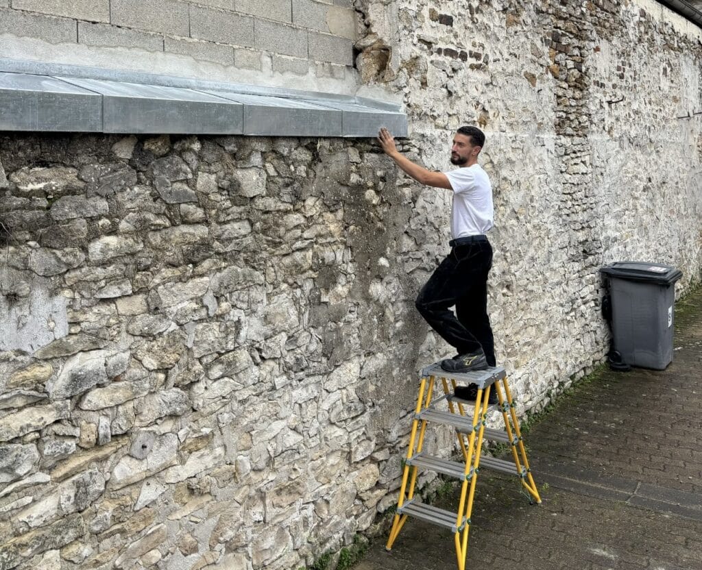 Un couvreur 78 effectuant la pose de zinguerie pour l'étanchéité d'un mur en pierre.